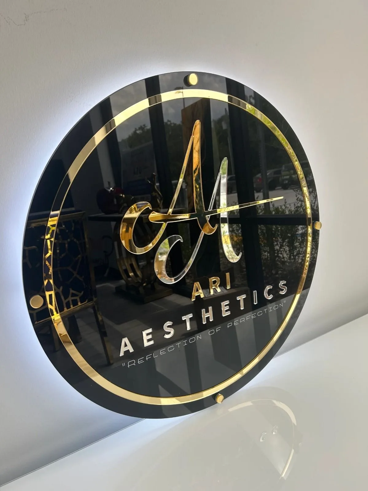 Round halo-lit logo plaque in gold and black acrylic for an aesthetics clinic reception