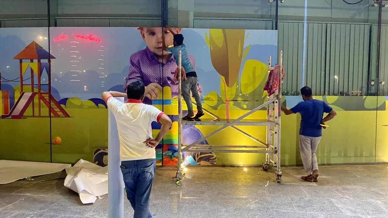 Bayan Signage installers applying a large printed wall mural from a scaffold tower in the UAE