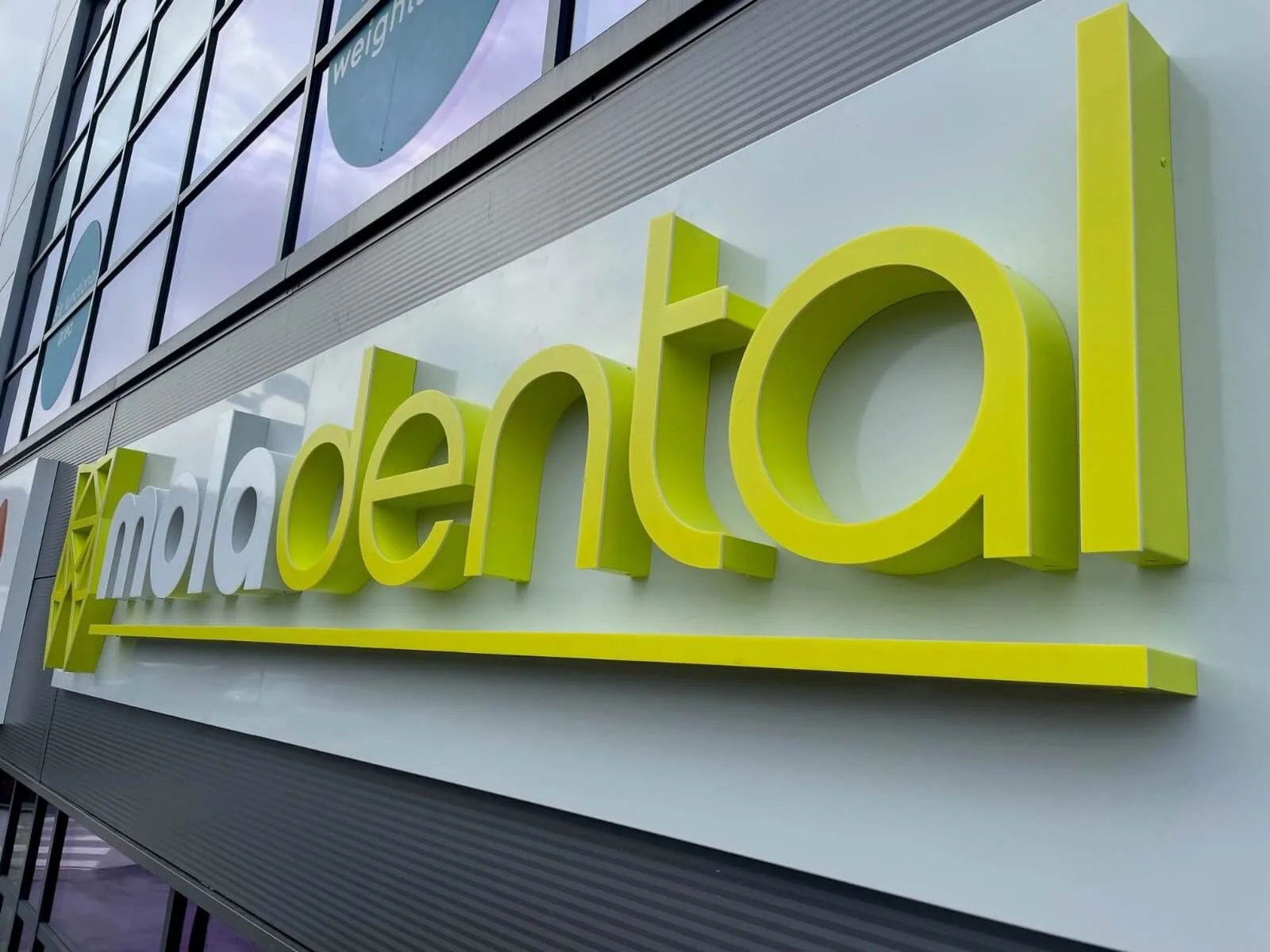 Lime green 3D letters installed on the light facade of a dental clinic
