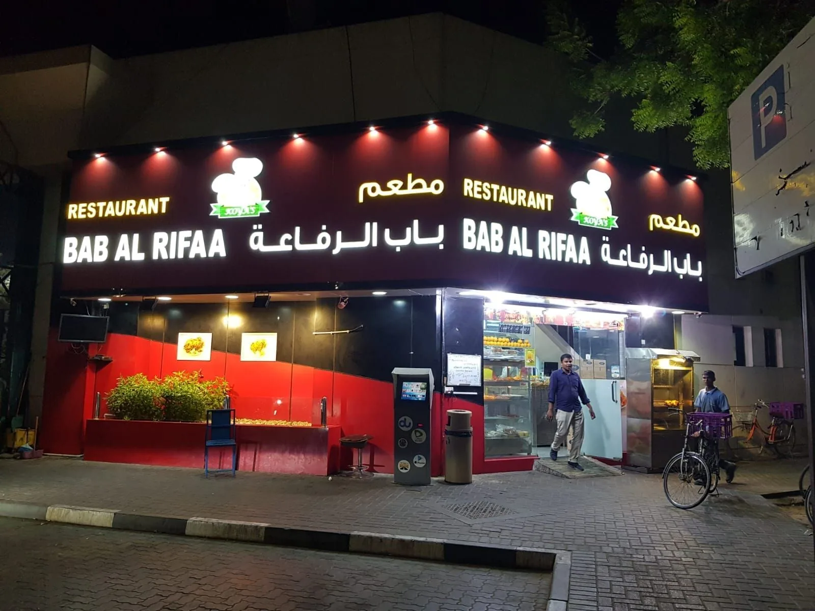 Bilingual Arabic and English front-lit letters on a restaurant fascia at night