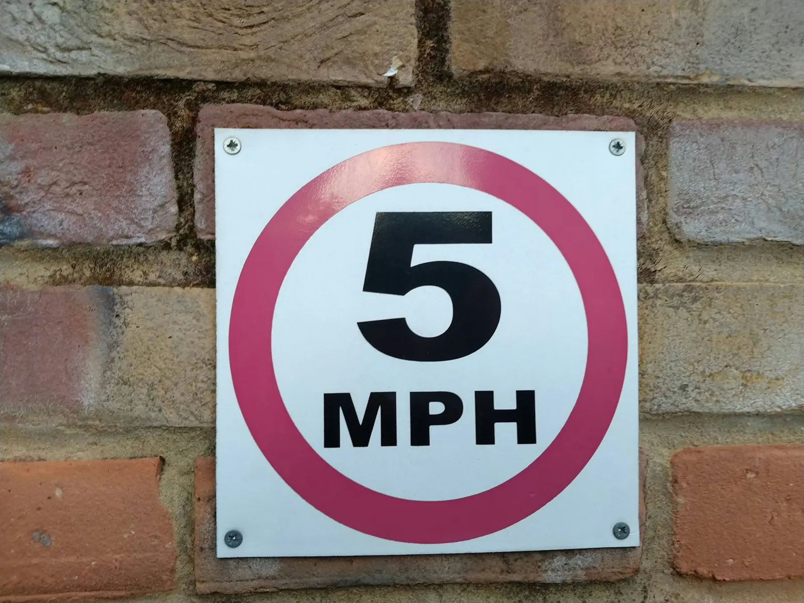 Flat aluminium sign plate with a 5 MPH speed limit fixed to a brick wall