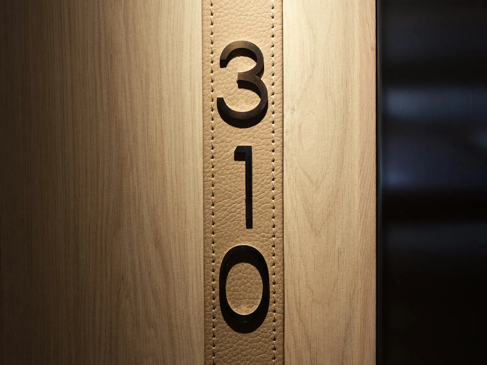 Black metal apartment number signs reading 310 mounted vertically on a wooden door frame
