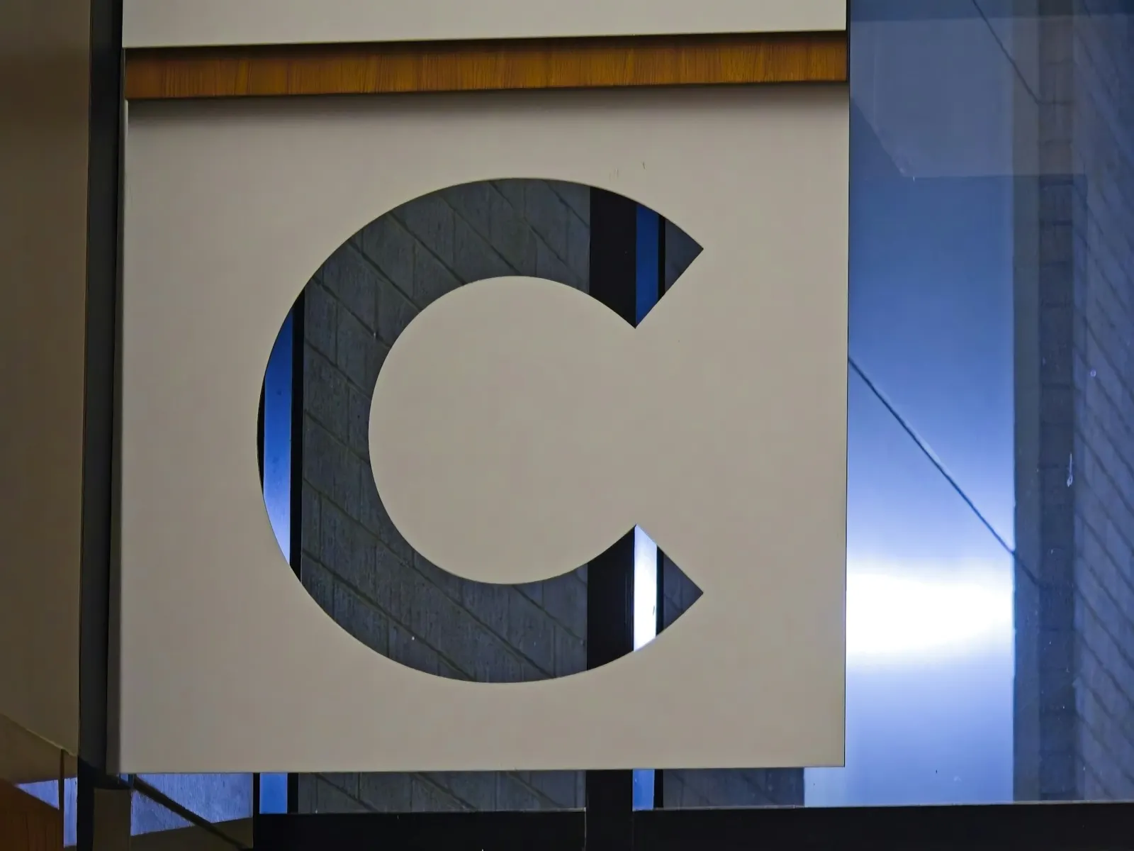 Architectural signage panel with cut-out hall letter mounted on a glass and steel facade