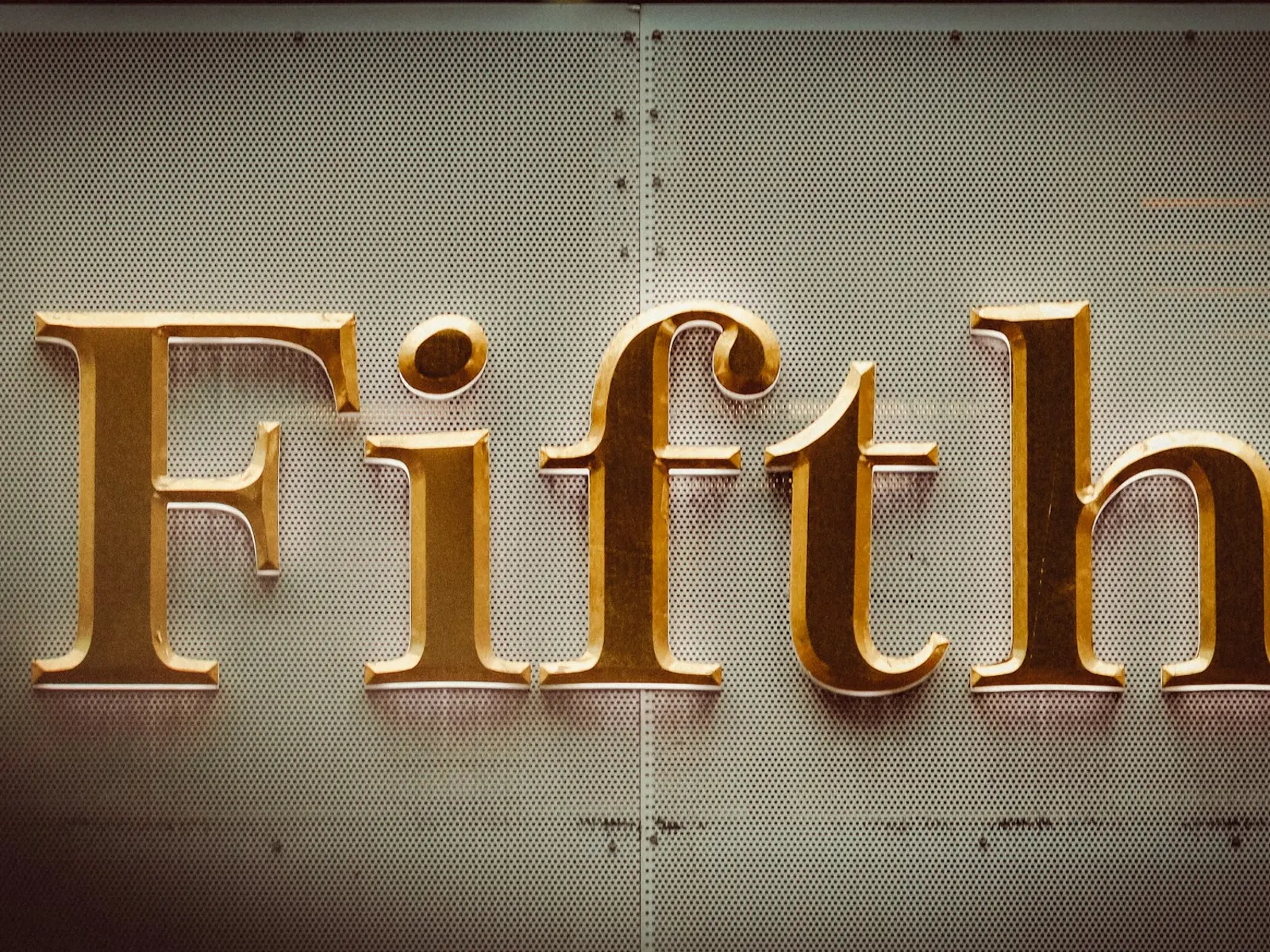 Polished brass 3D letters spelling Fifth mounted on a warmly lit wall