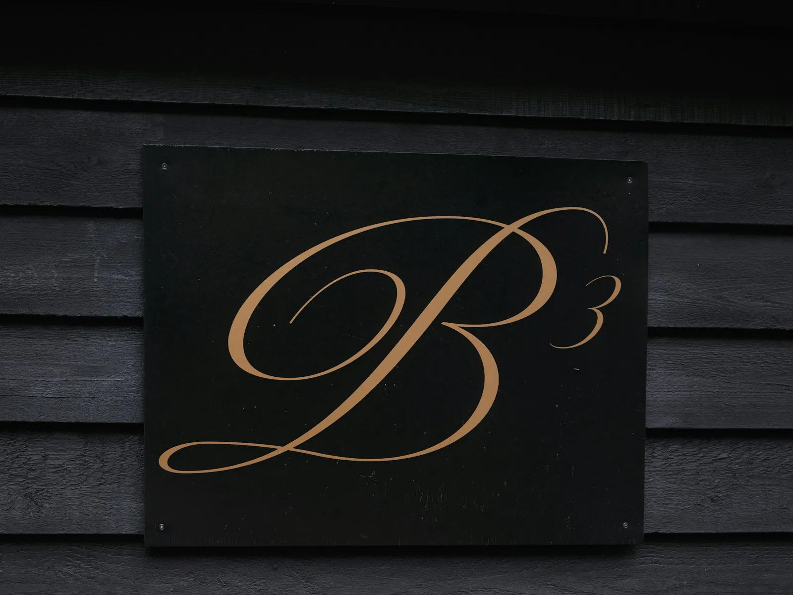 Black plate with a gold script monogram mounted on a dark timber-clad wall