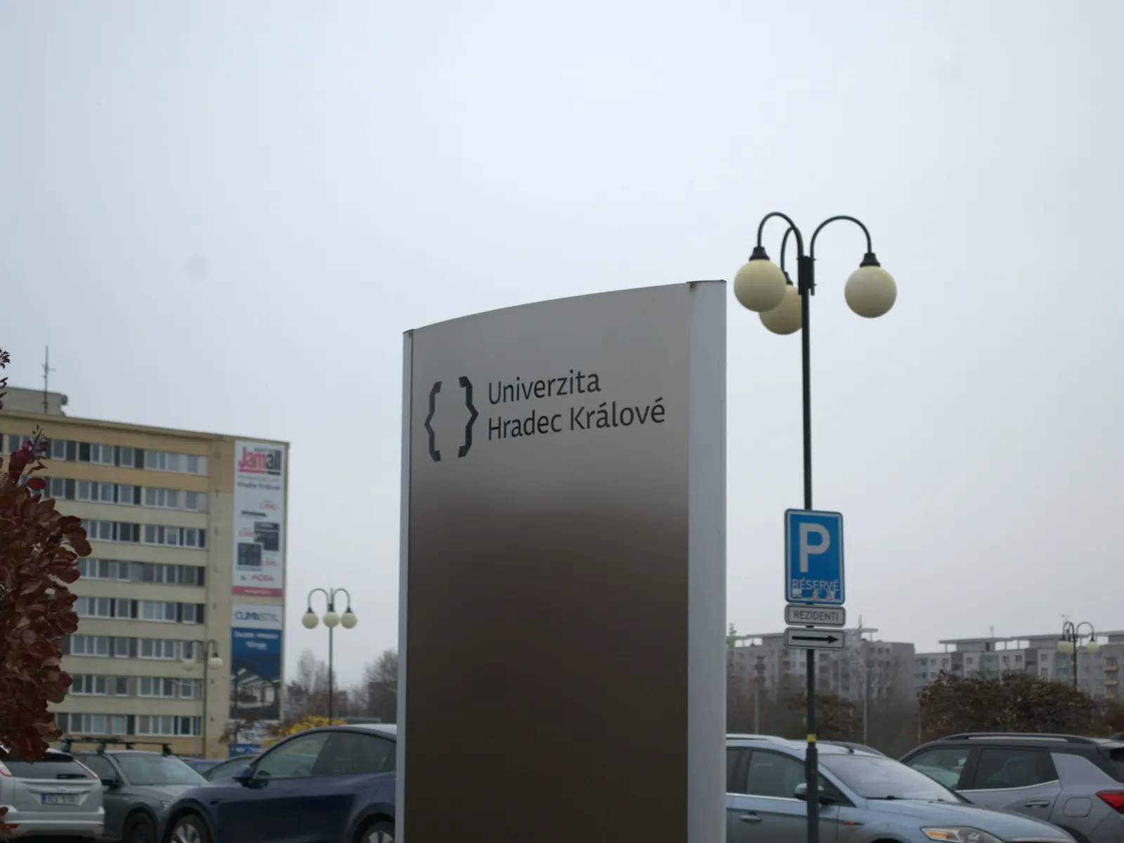 Modern brushed metal campus wayfinding totem at a university entrance beside a car park