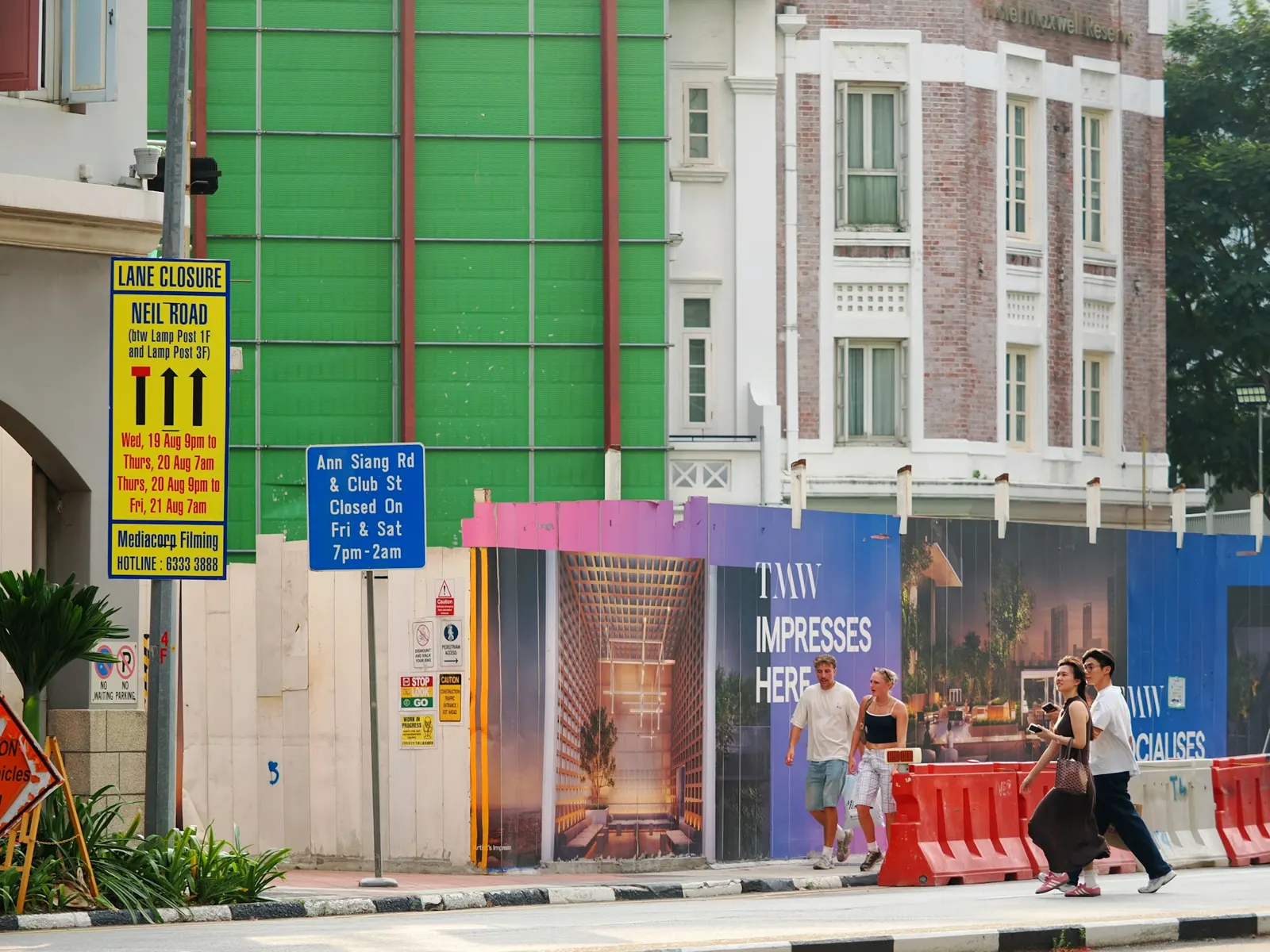 Construction site hoarding with printed project boards along a city pavement