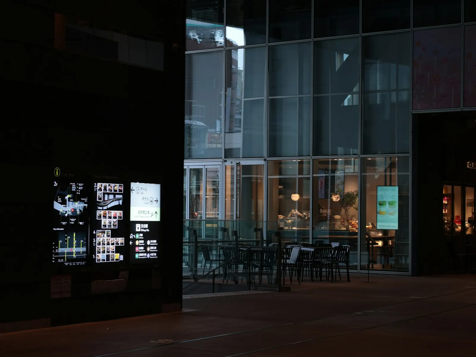 Glowing building directory display with floor map beside a glass-walled cafe at night