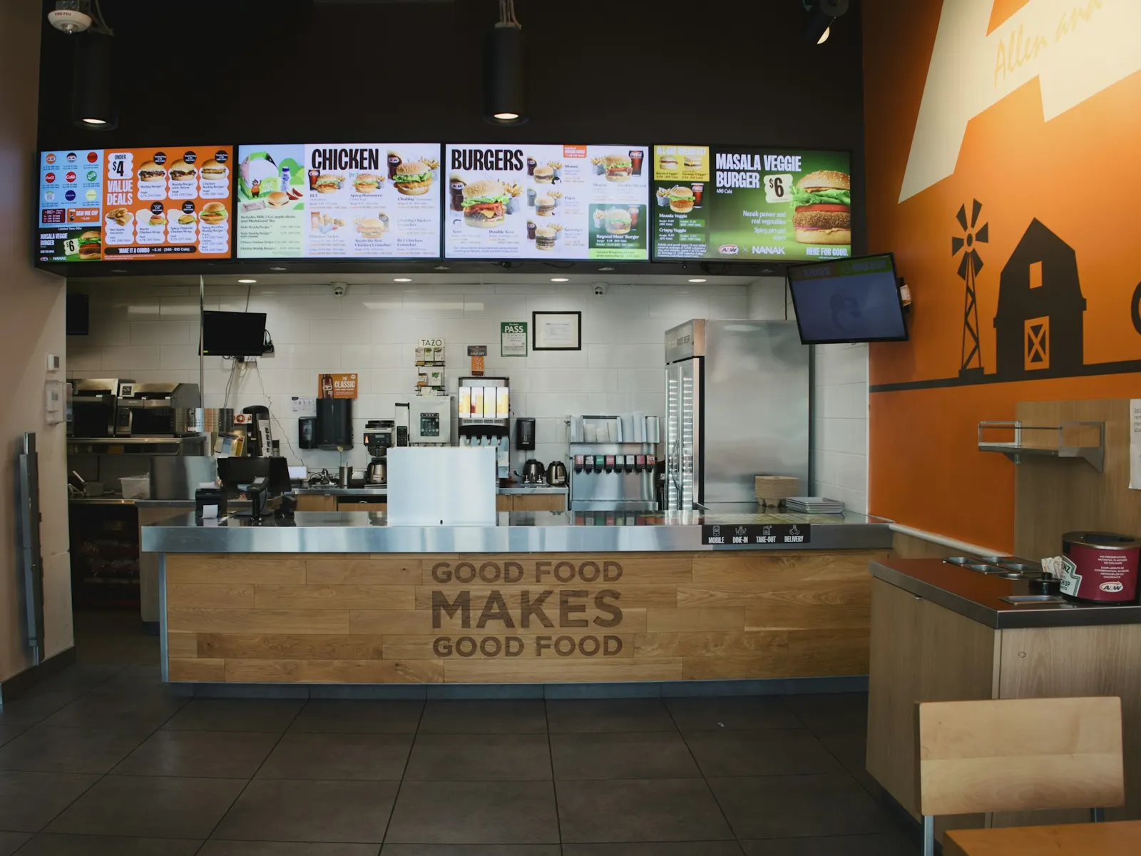 Row of digital menu board screens showing food photos above a fast food service counter
