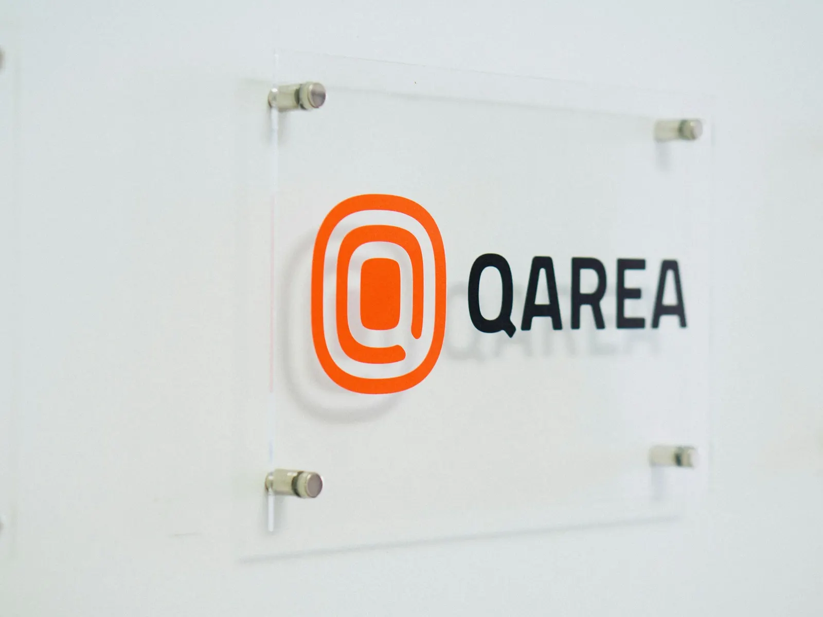 Clear acrylic door name plate with a printed logo fixed on polished stand-offs to a white wall