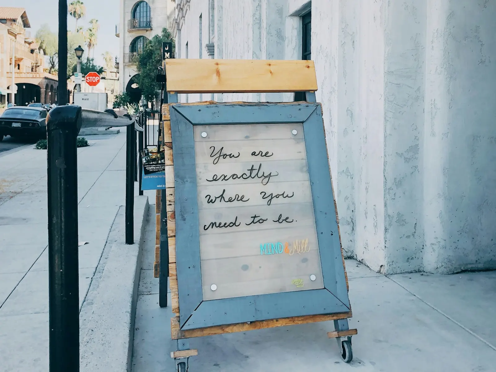 Wooden framed sidewalk easel sign standing on a sunny pavement outside a shop