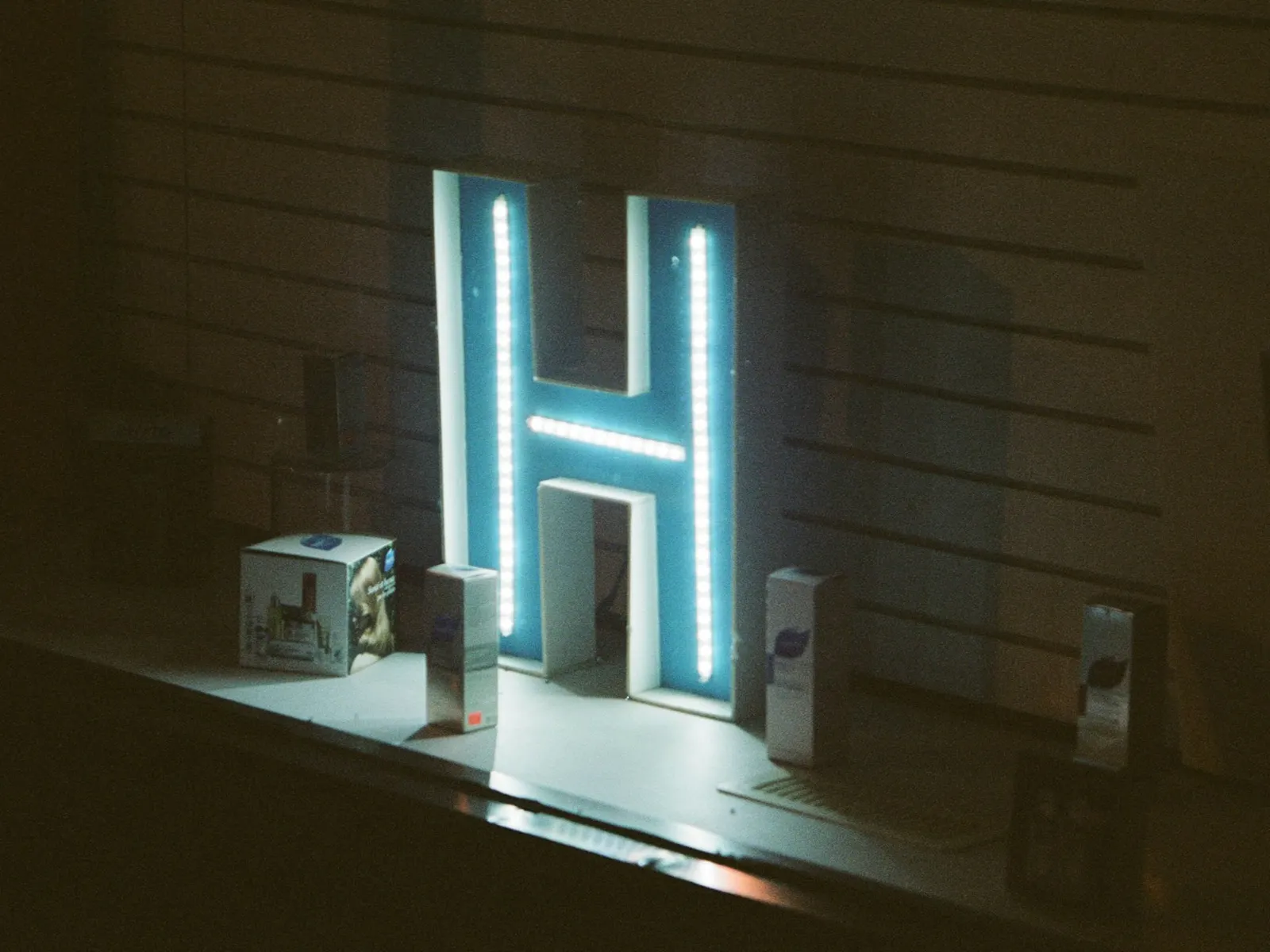 Glowing edge-lit letter H with bright light outlining its acrylic edges at night