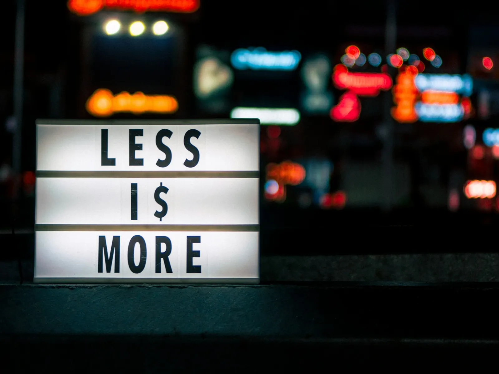Illuminated light box sign with black letters glowing against blurred city lights at night