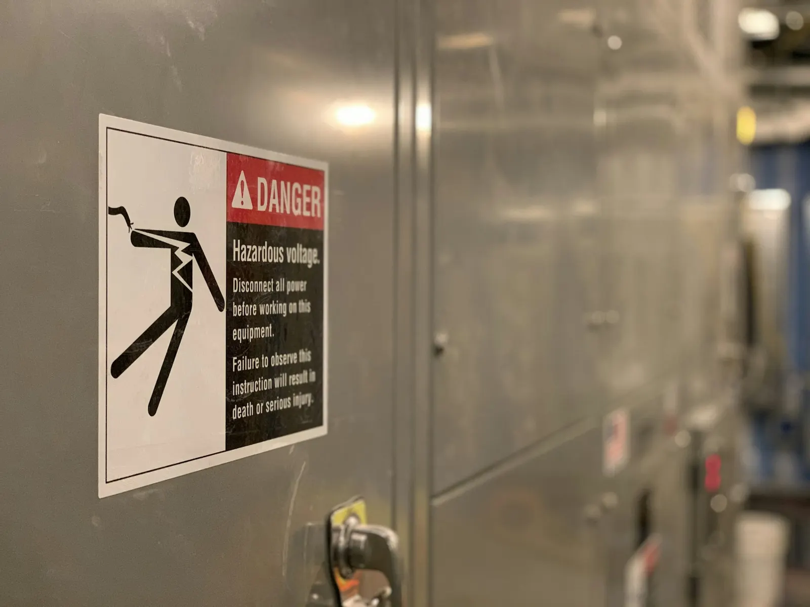 Danger hazardous voltage warning sign fixed to grey electrical switchgear cabinets
