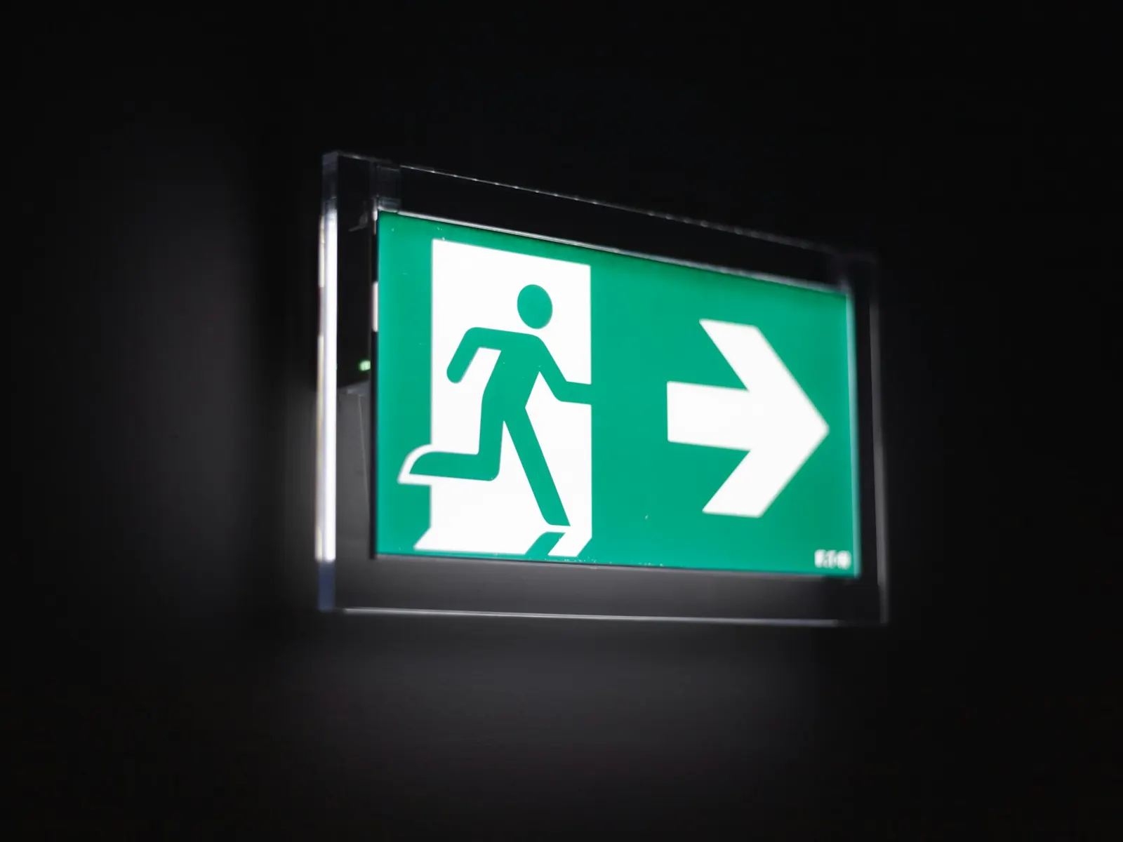 Illuminated green emergency exit sign with running figure and arrow on a dark wall