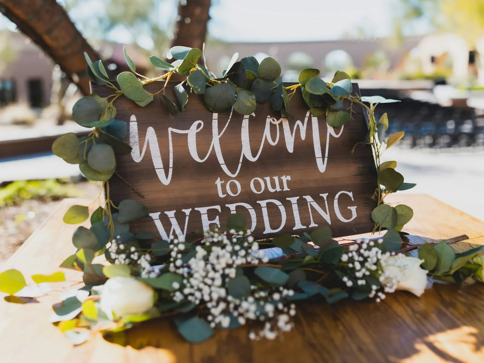 Rustic wooden event welcome sign decorated with eucalyptus and white flowers on a table