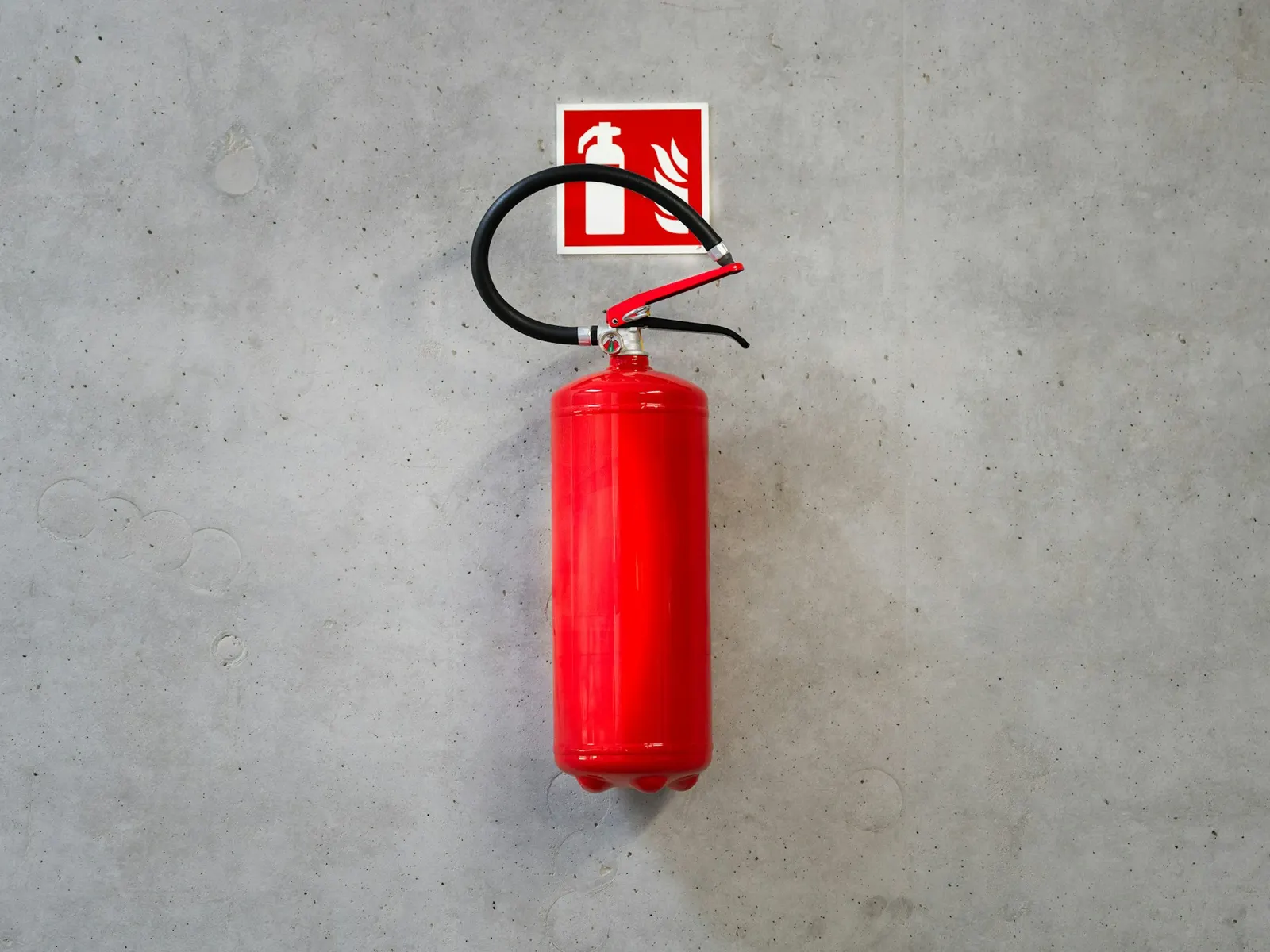 Red fire extinguisher sign mounted above a wall-hung extinguisher on bare concrete
