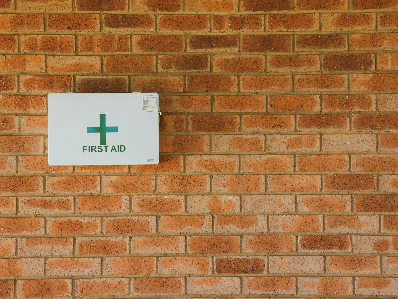 Green and white first aid sign with cross mounted on a red brick wall