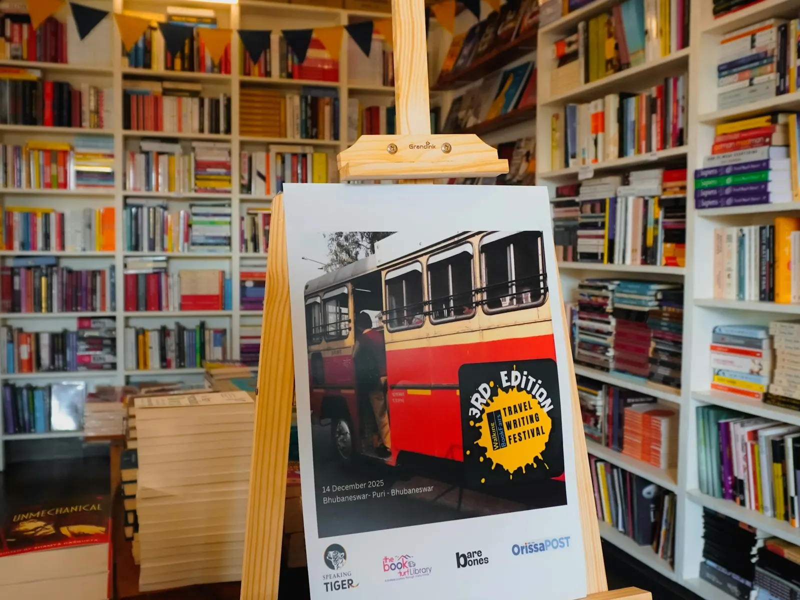 Printed foam board poster displayed on a wooden easel inside a bookshop
