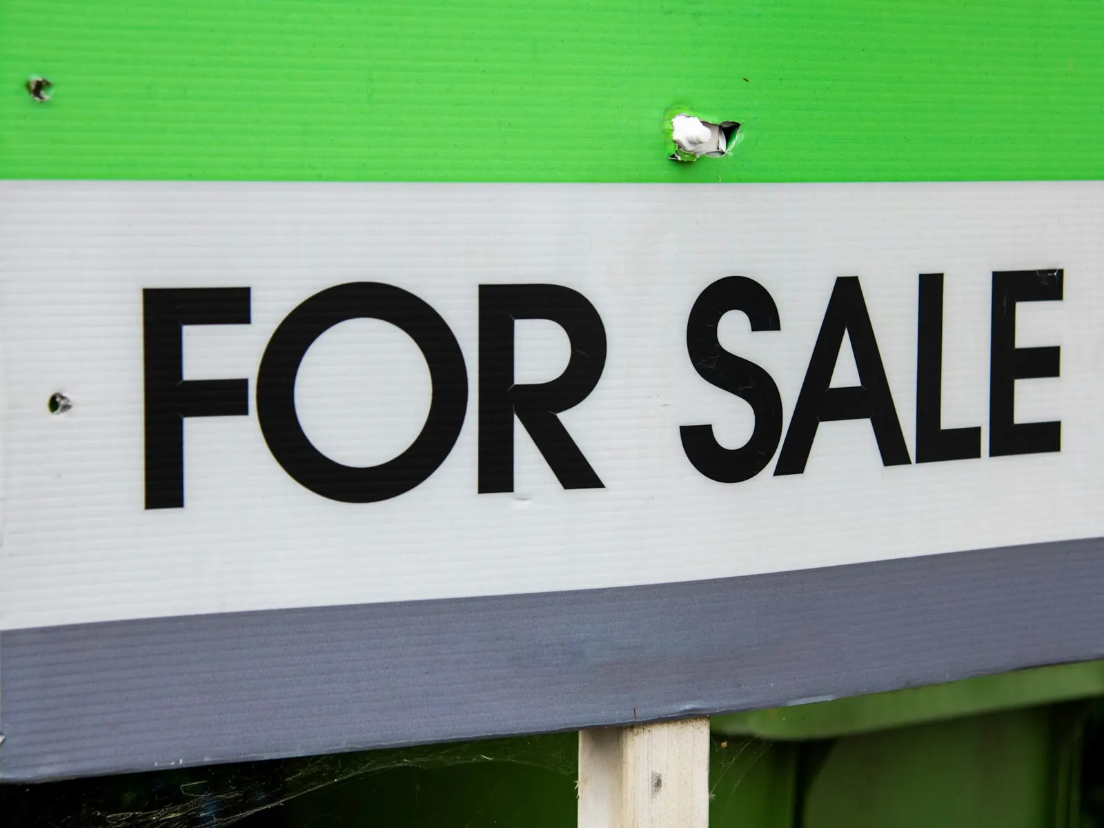 Close-up of a green and white FOR SALE sign board mounted outdoors on a post