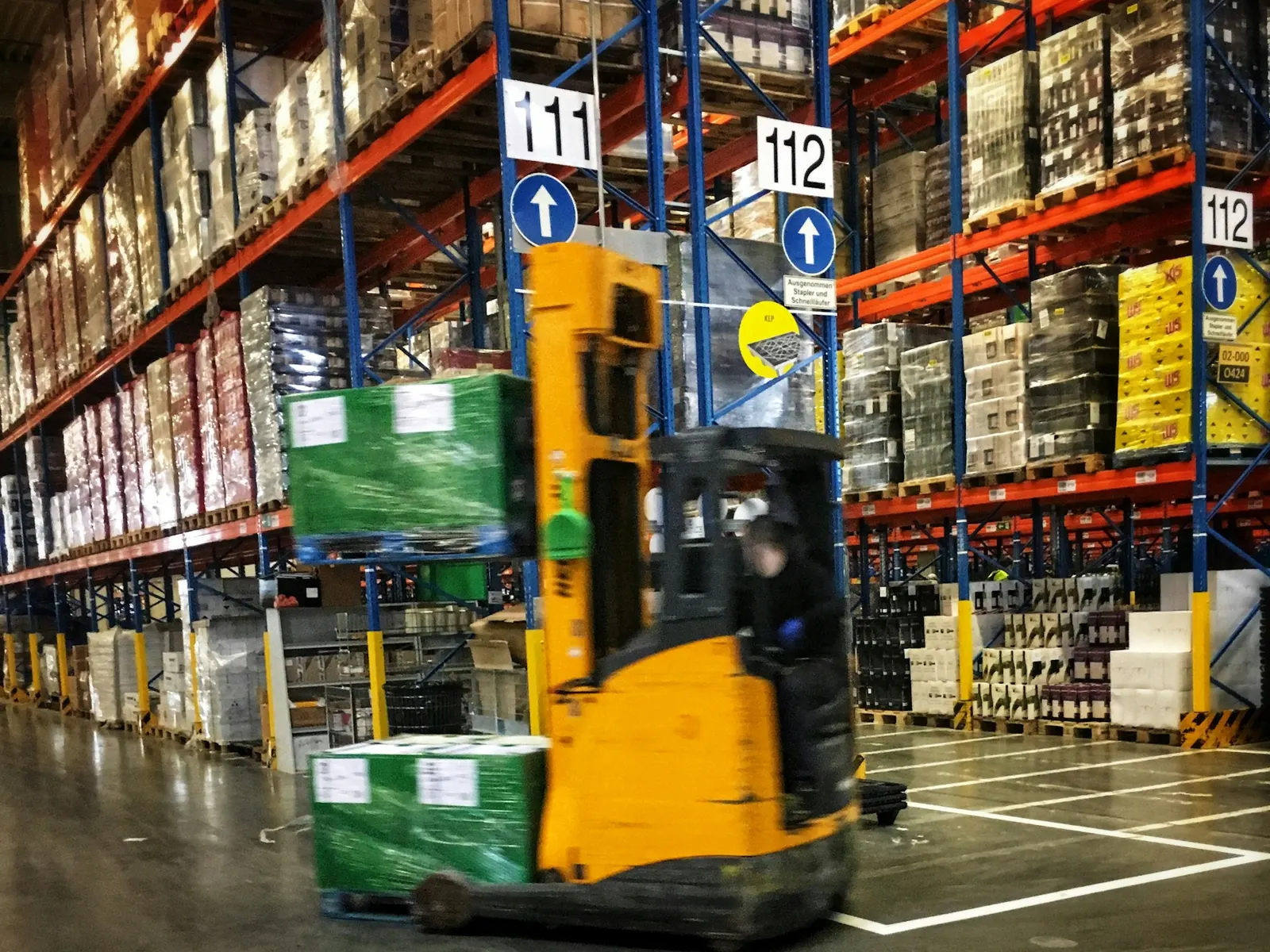 Forklift moving through a warehouse aisle of tall pallet racking with numbered aisle signs