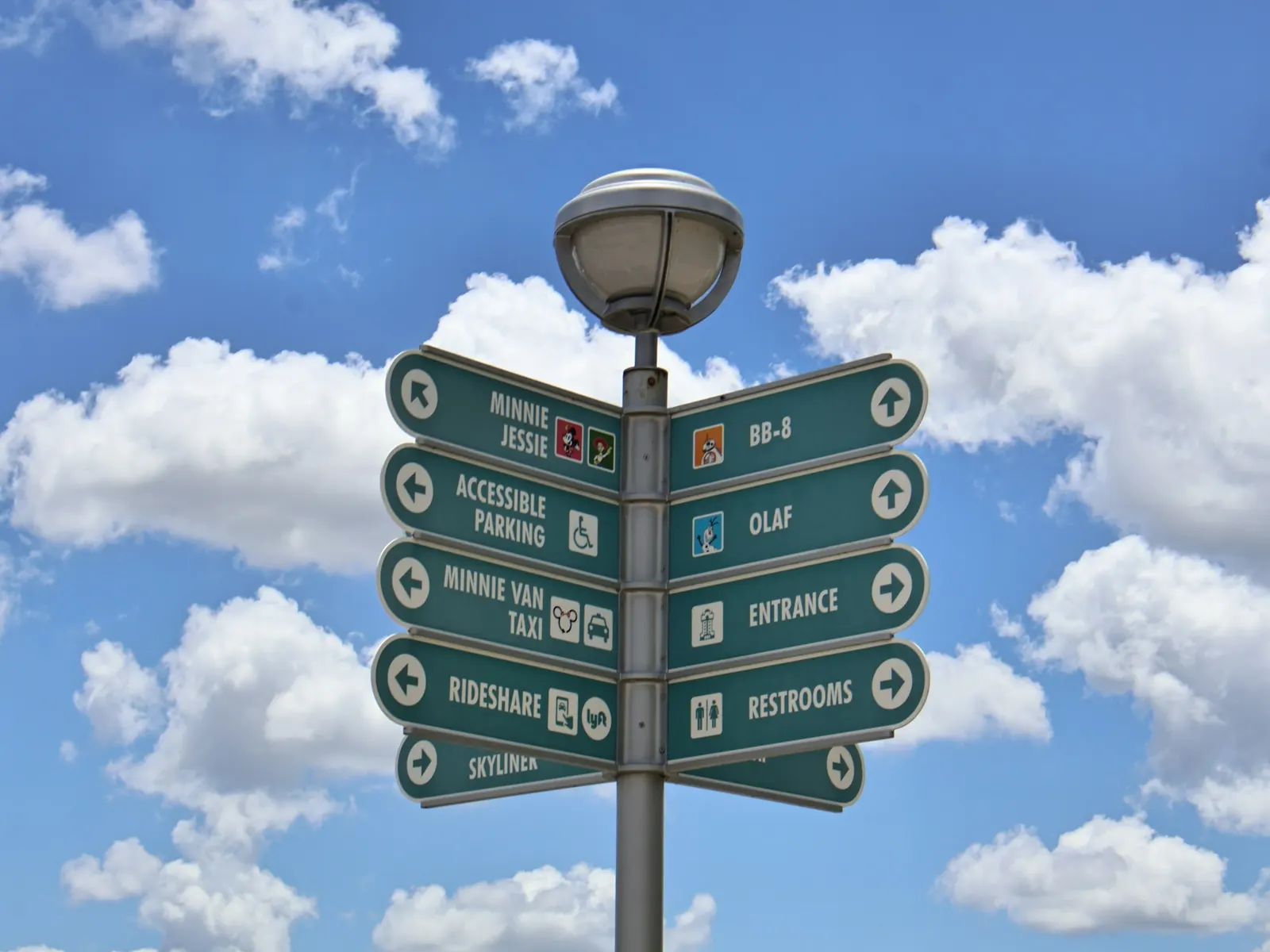 Freestanding directional sign post with multiple arrow panels and a lamp against a blue sky