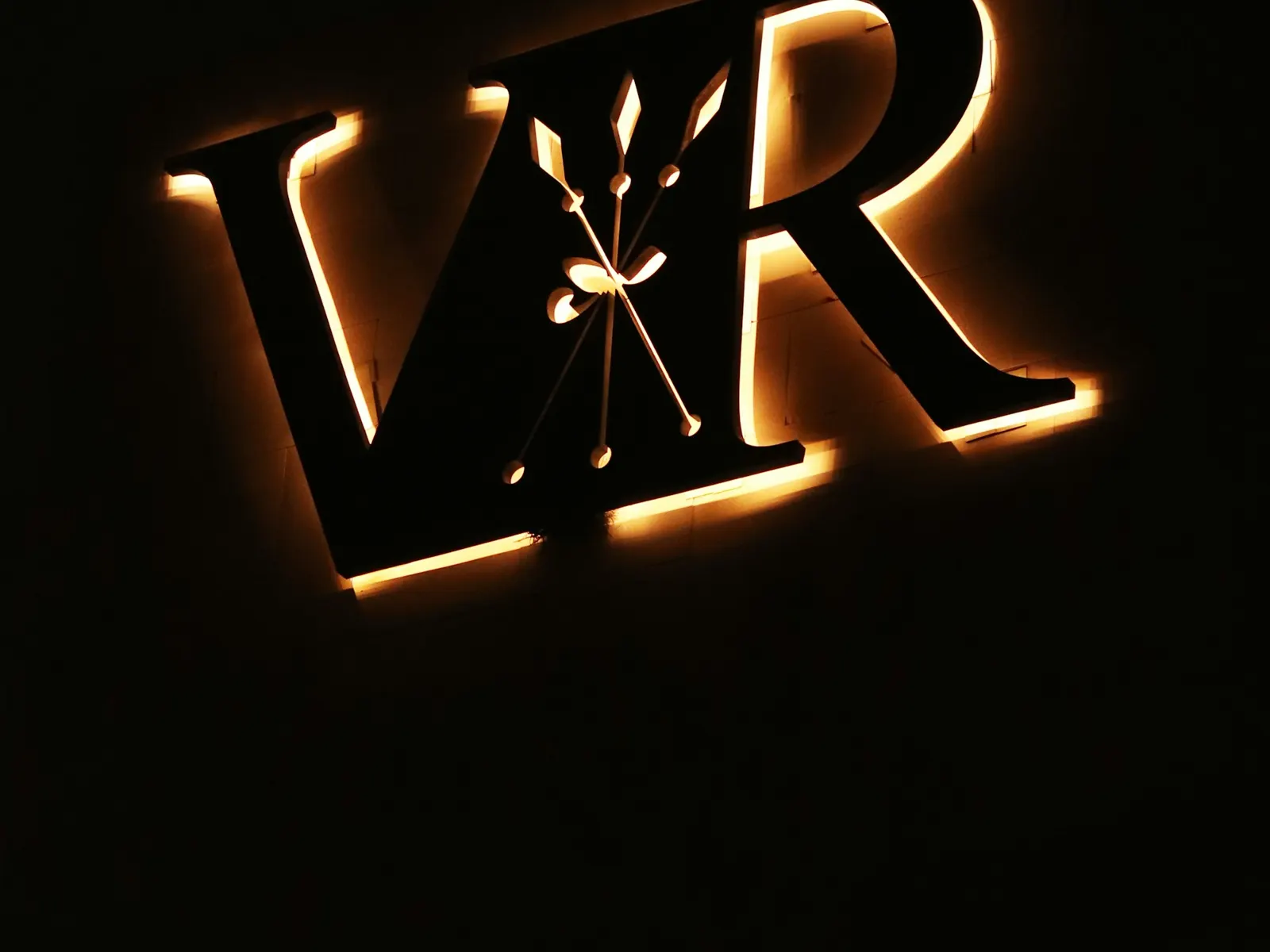 Halo-lit dark metal letters with a warm amber glow on a black wall at night