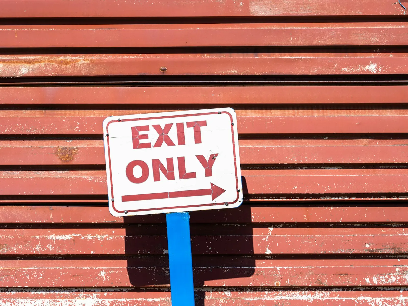 White steel sign board reading Exit Only on a post against corrugated metal
