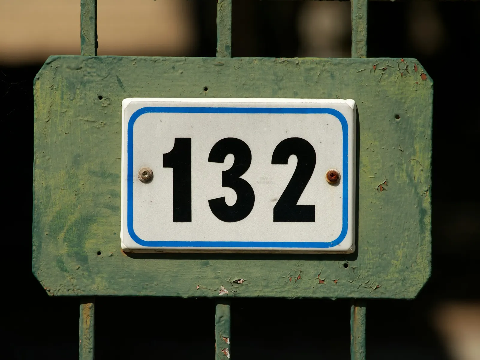 White enamel gate number sign reading 132 fixed to a green metal gate