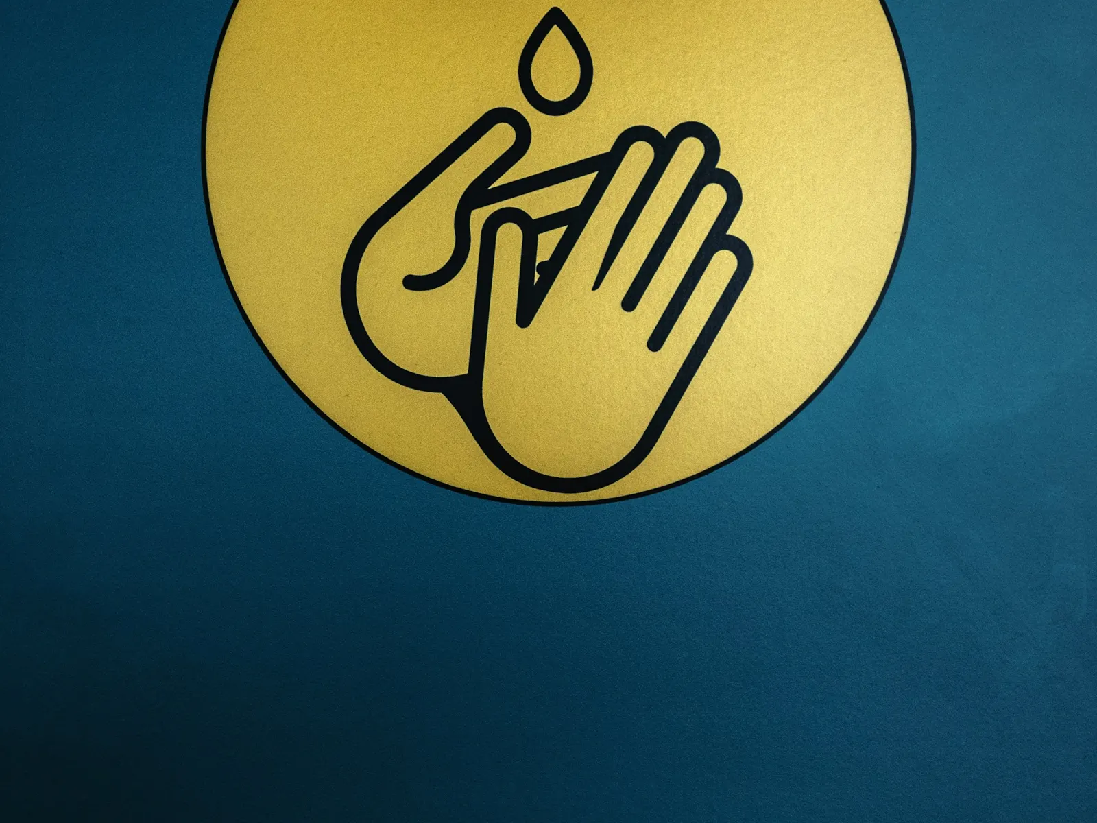 Infection control sign with gold hand washing symbol mounted on a dark teal wall