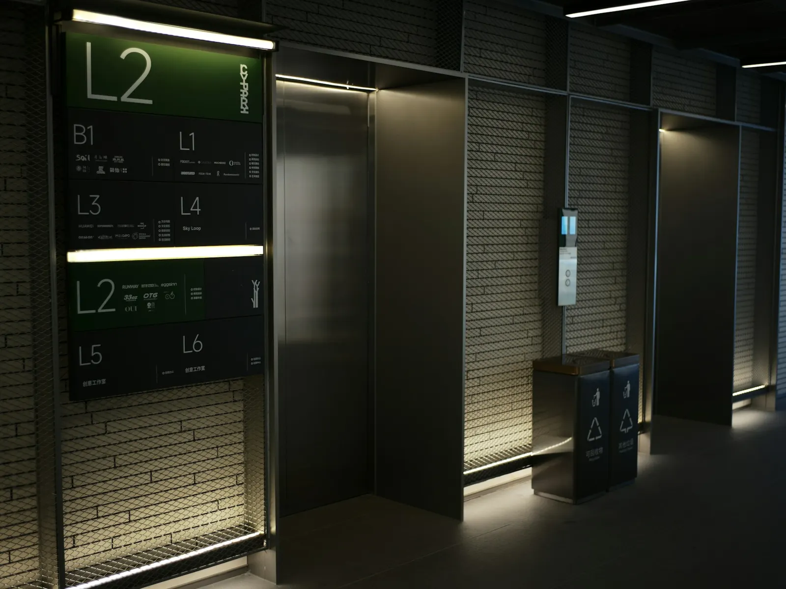 Illuminated floor directory sign listing levels beside lifts in a modern building lobby
