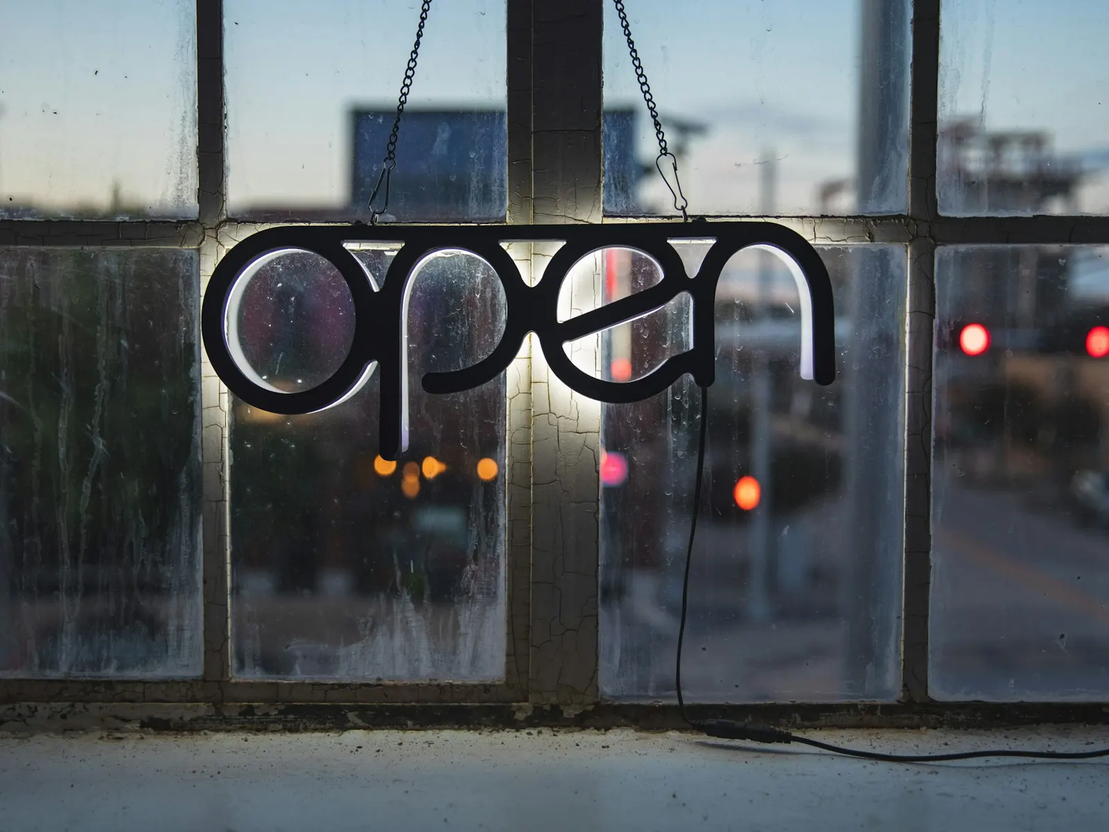 Illuminated LED open sign hanging in a shop window at dusk