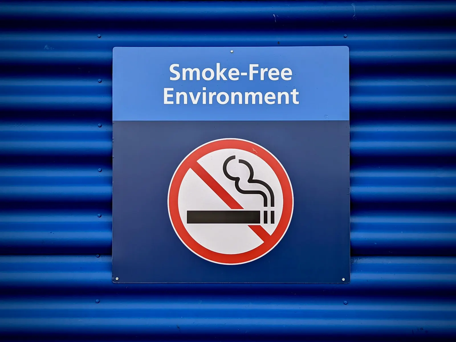 Smoke-free environment no smoking sign mounted on a blue corrugated metal wall