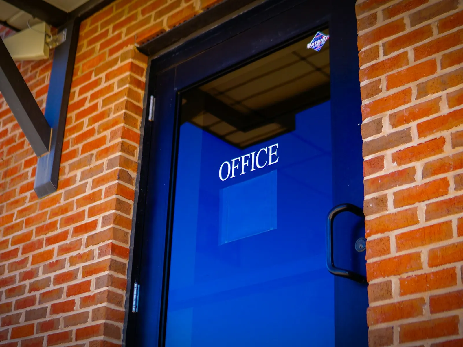 Blue office door with white OFFICE sign lettering on glass in brick wall