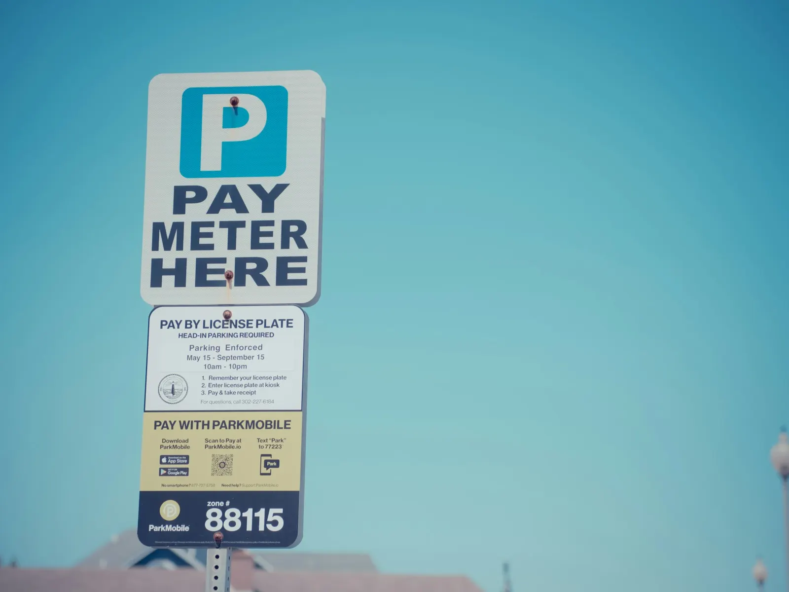 Pay meter here parking sign with payment and tariff information panels on a post