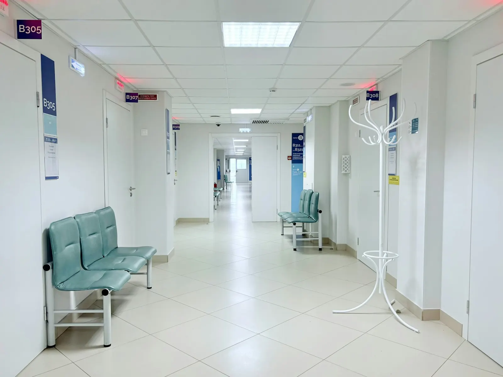 Bright hospital corridor with patient room signs mounted beside doors and waiting seats