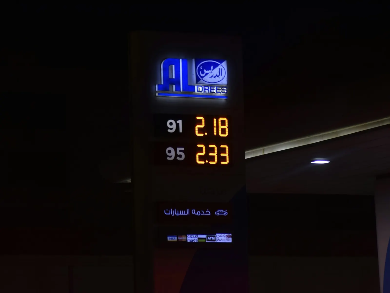 Illuminated petrol station price pylon showing 91 and 95 fuel prices at night