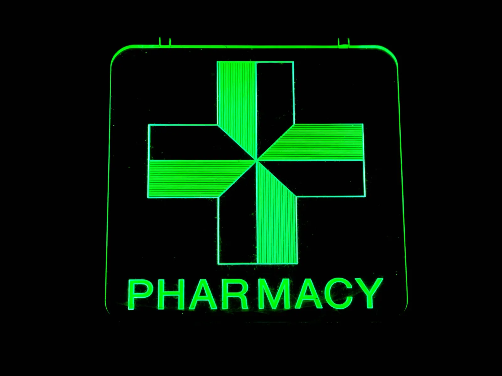 Illuminated green pharmacy cross sign with glowing PHARMACY lettering against a dark night background