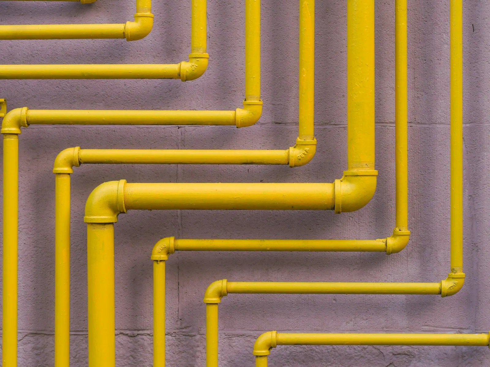 Colour-coded yellow gas pipes running in parallel bends along a wall