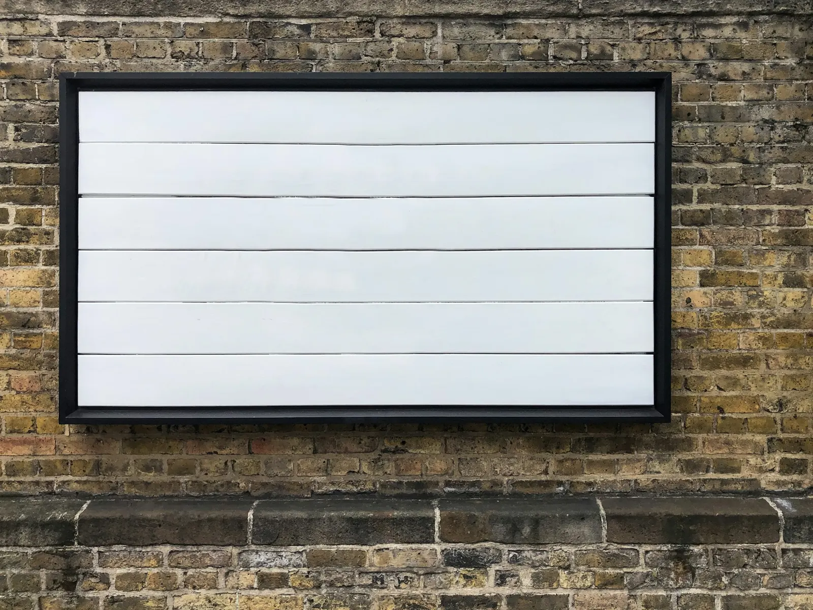 Blank white panel sign in a black frame mounted on a weathered brick wall