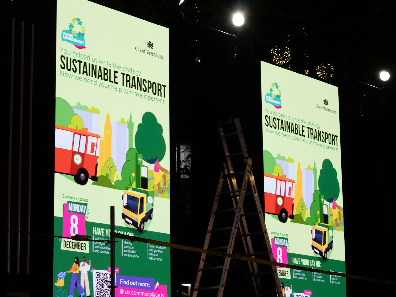 Two tall illuminated printed display stands with event graphics standing in a dark venue