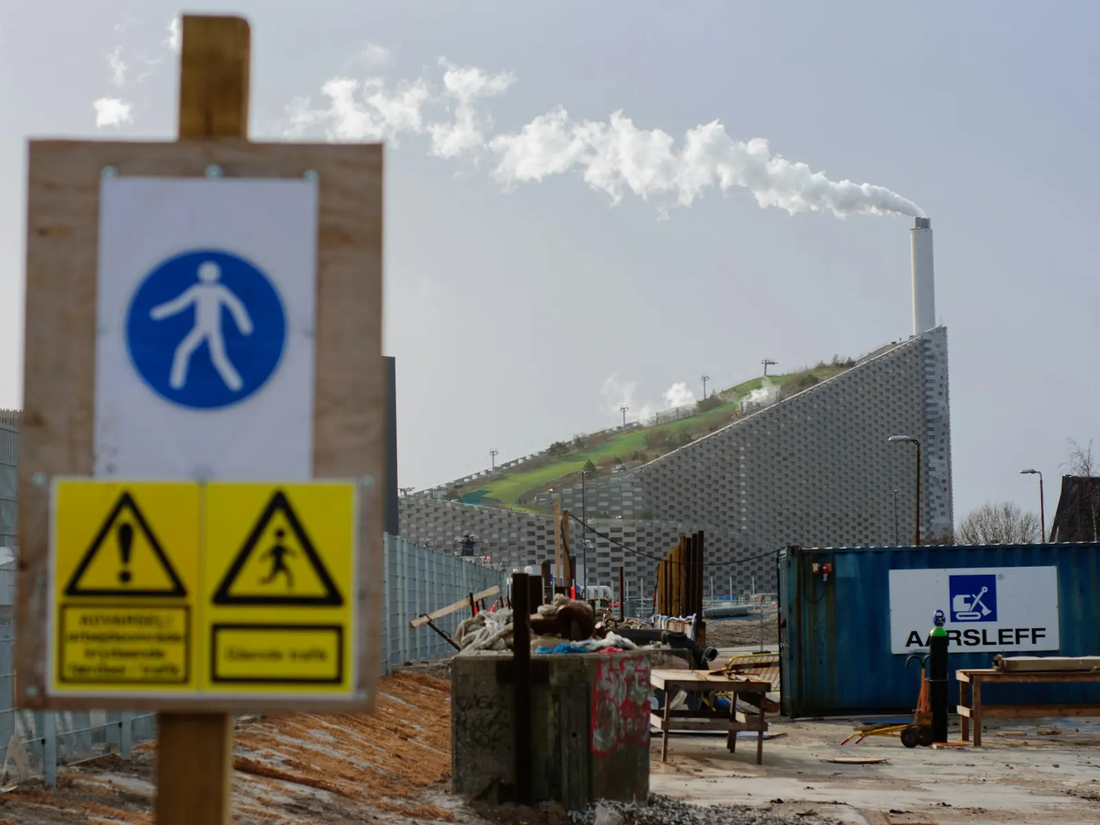 Construction site information board with safety signs on a timber post beside a building site