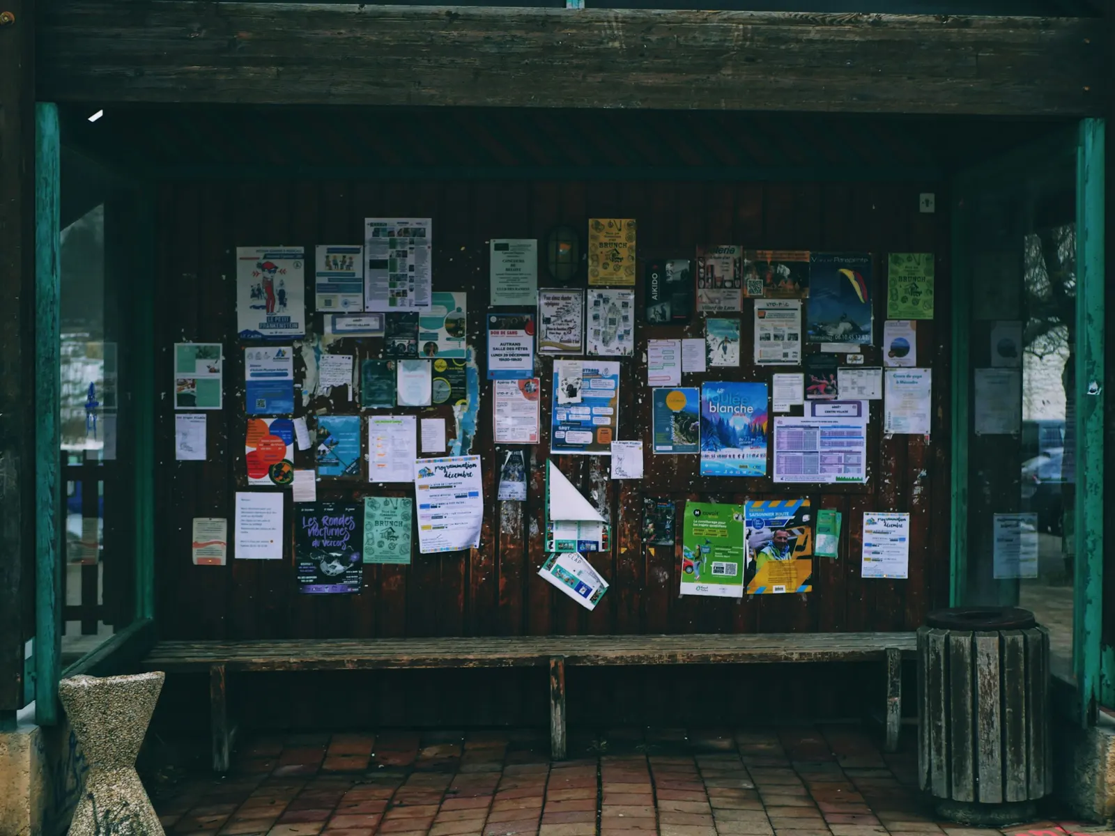 Outdoor public notice board covered with posters inside a covered wooden shelter