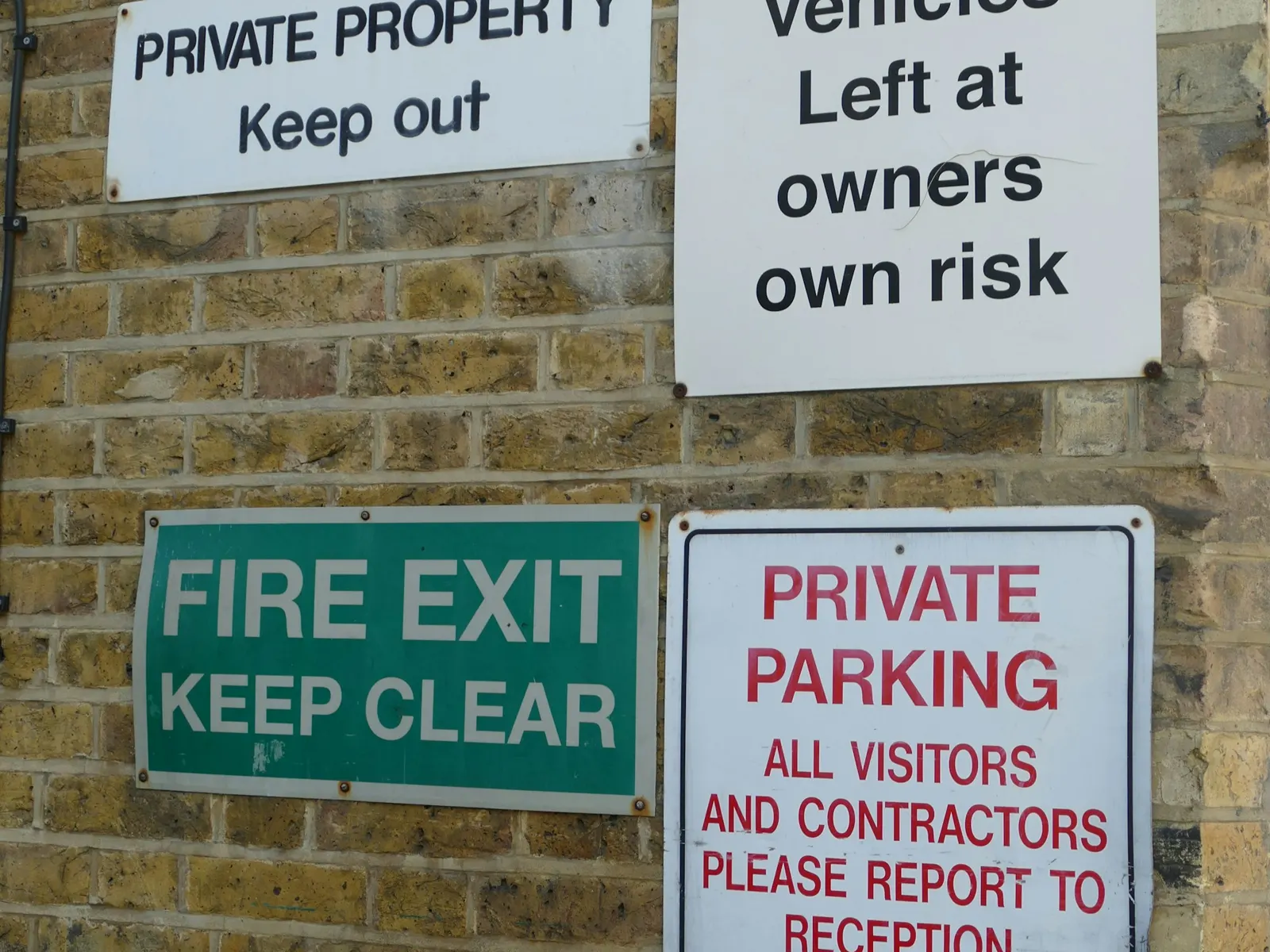 Printed flat board signs for parking, fire exit and private property on brick