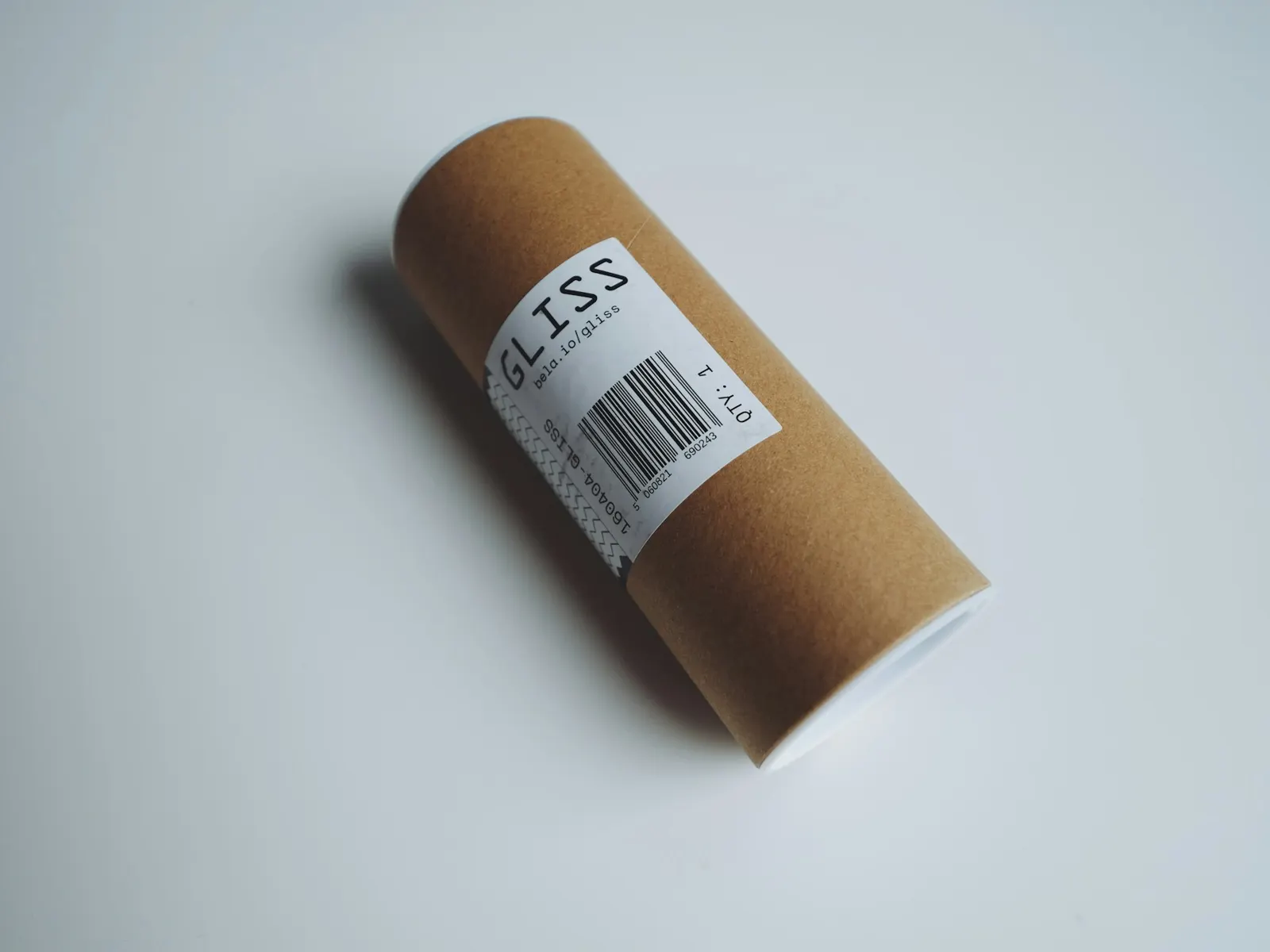 Printed barcode asset label wrapped around a cardboard tube on a pale grey surface