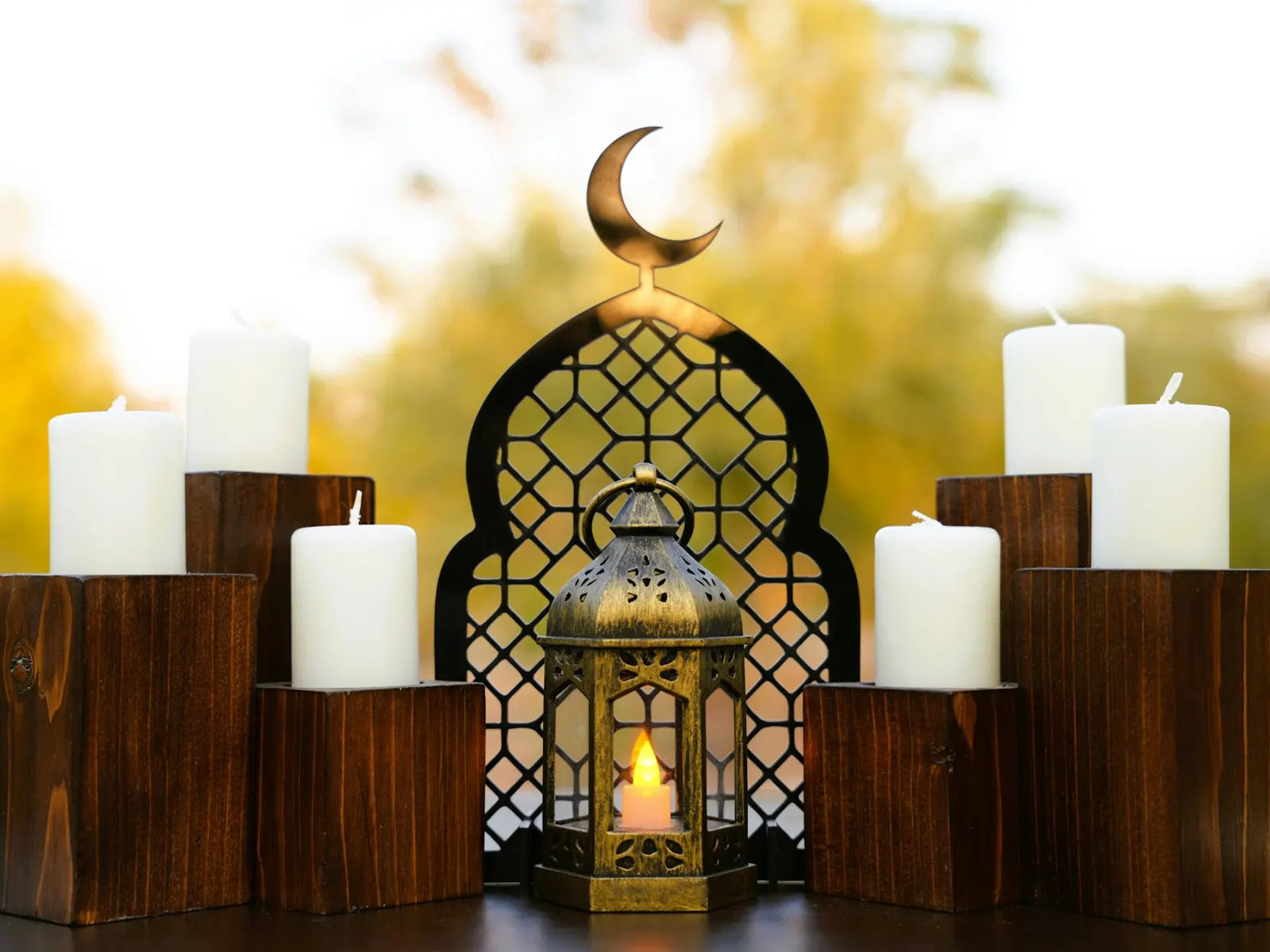 Ramadan decoration with crescent moon arch, glowing lantern and white candles on wooden blocks