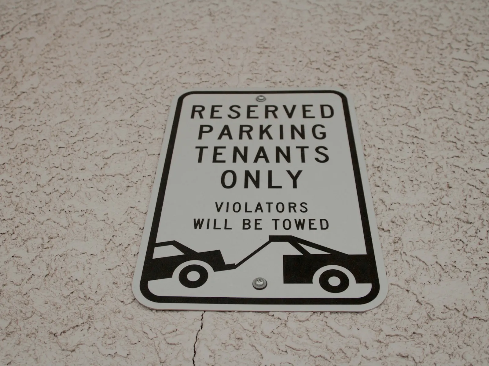 Reserved parking tenants only sign with tow-away warning fixed to a textured wall