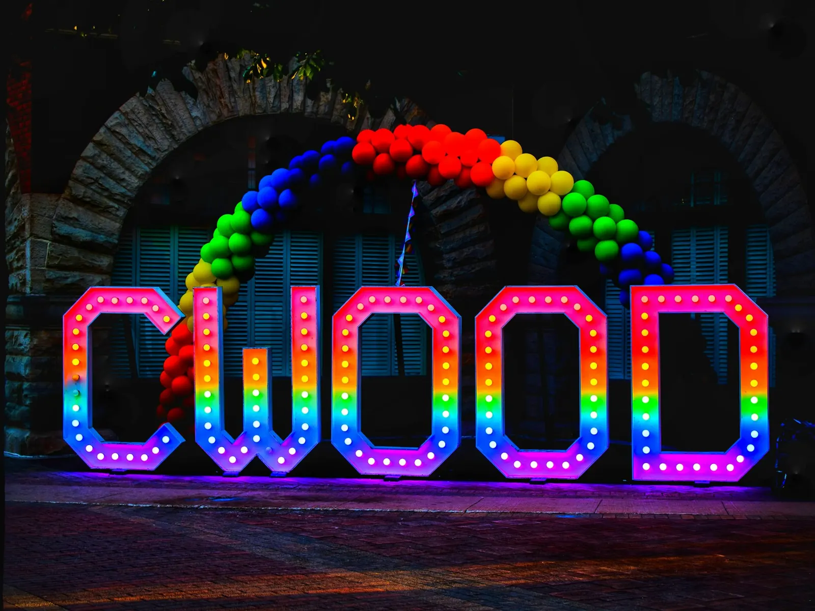 RGB LED letter sign glowing in rainbow colours at night under a balloon arch