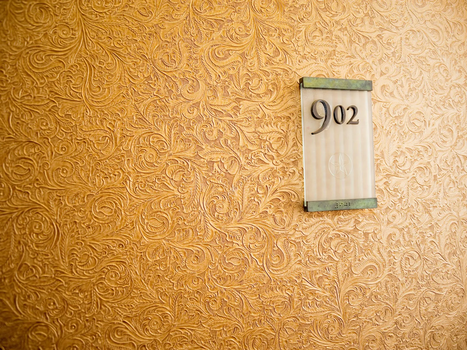 Frosted acrylic room number sign reading 902 mounted on a textured corridor wall