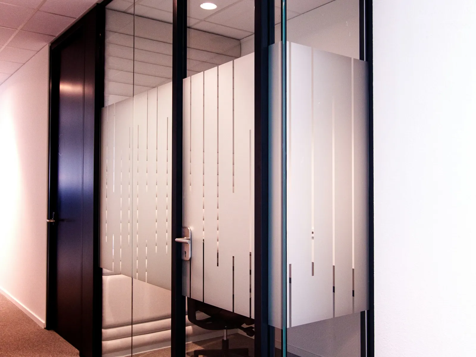 Glass meeting room walls with sandblast effect film stripes in a modern office corridor